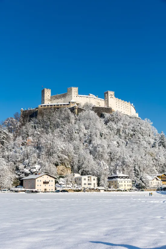 Festung Hohensalzburg auf verschneitem Hügel über Salzburg mit blauem Winterhimmel